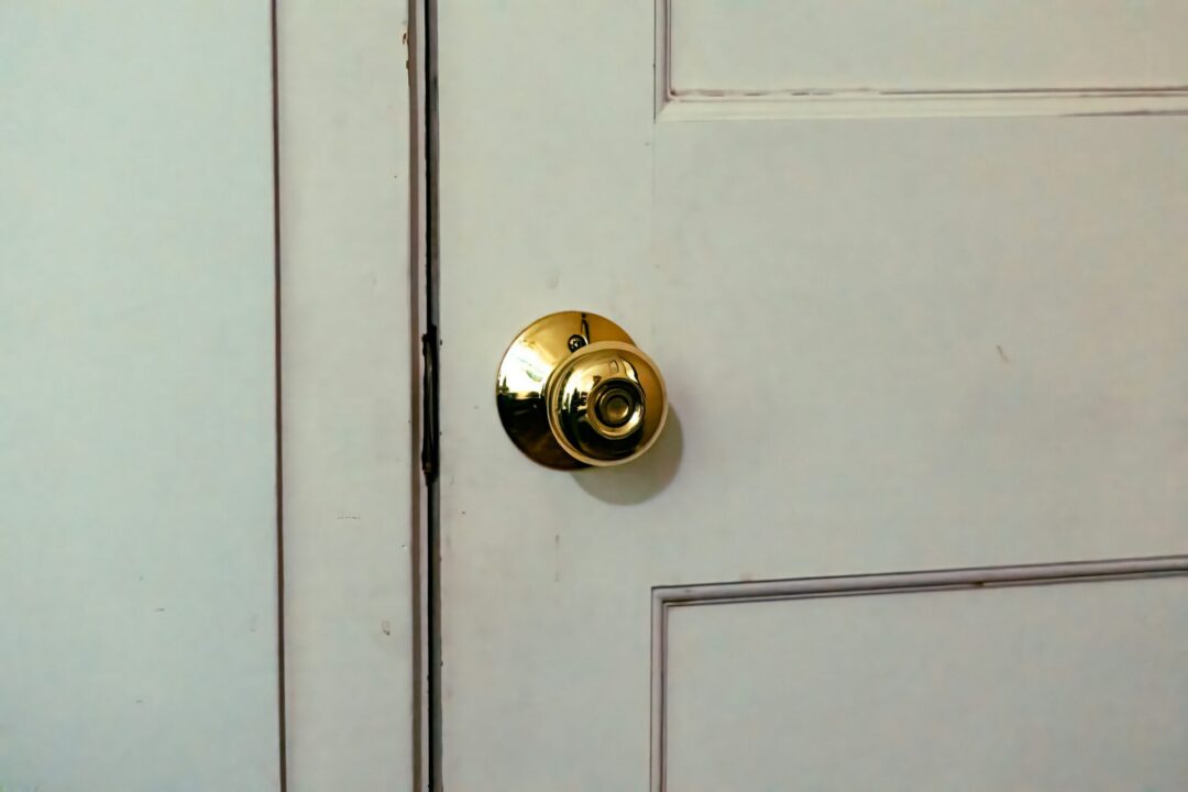 アンティーク調の写真。クリームがかった木製ドアにピカピカに輝く黄金のドアノブ。メッキのようにも見えるが撮影者側まで映り込むほどピカピカに磨かれている。