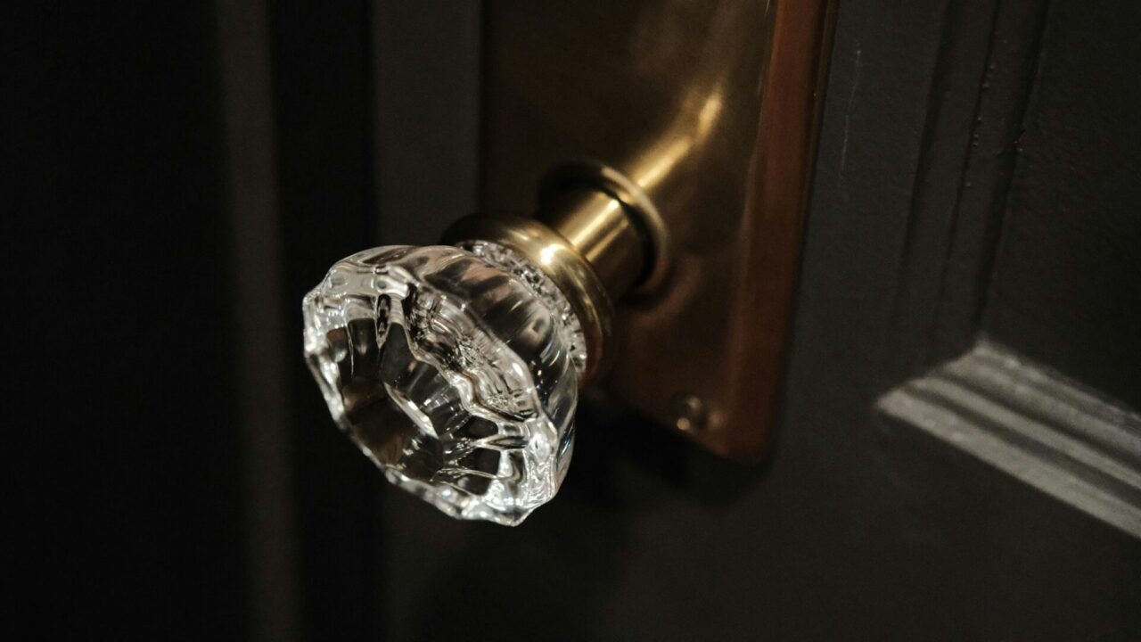 アンティーク調の写真。焦げ茶色の木のドアに透明でキラキラしたガラスのようなもので作られたドアノブ。ドアノブの根本も真鍮のようなものでできていて黄金色が美しい。