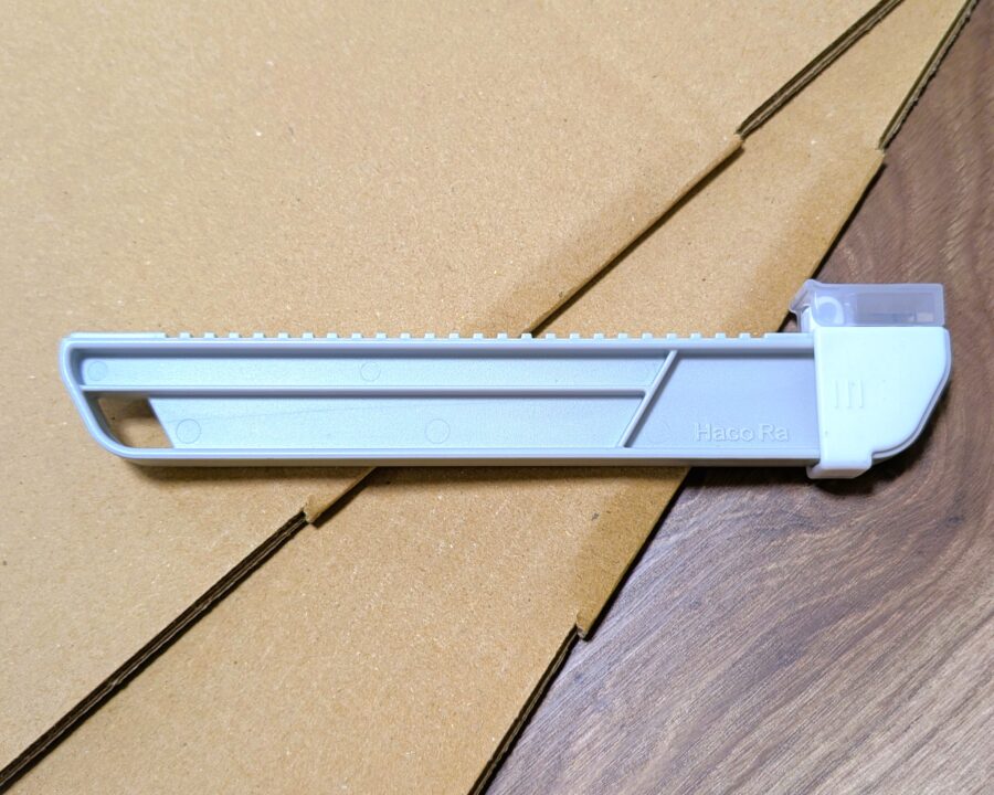 組み立て前のダンボール箱の上にダイソーのダンボールサイズ調整カッターが置いてある写真。